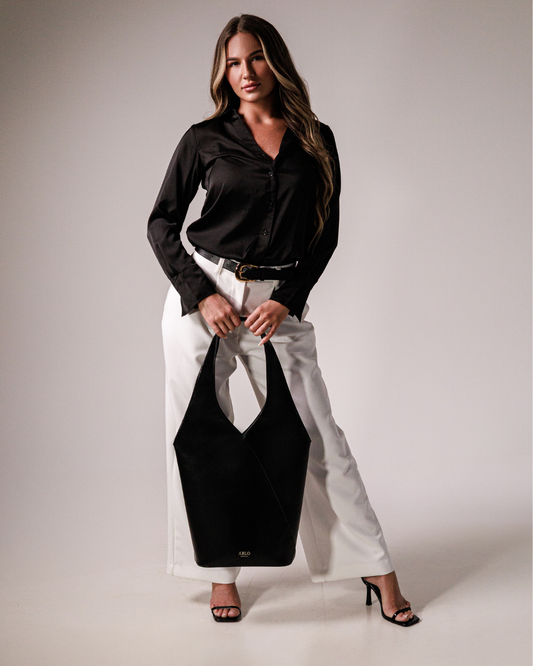 A professional woman holding a large shoulder bag for work, black, sophisticated, laptop carrier that is smart, sleek, stylish and has an ARLO london logo