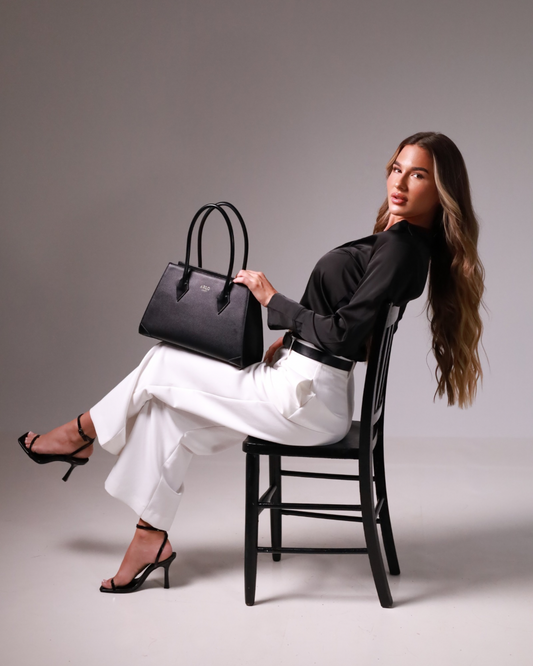 A pretty young professional woman holding a smart sophisticated simple black structured tote handbag for work and office use.